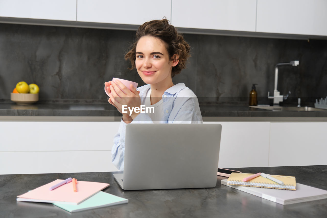 portrait of young woman using laptop while sitting on table