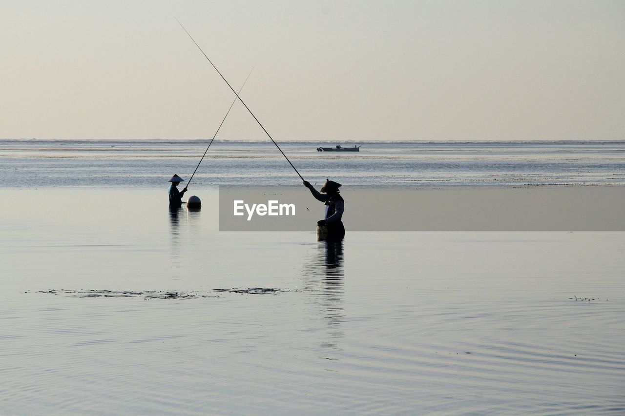 Men fishing in sea against clear sky