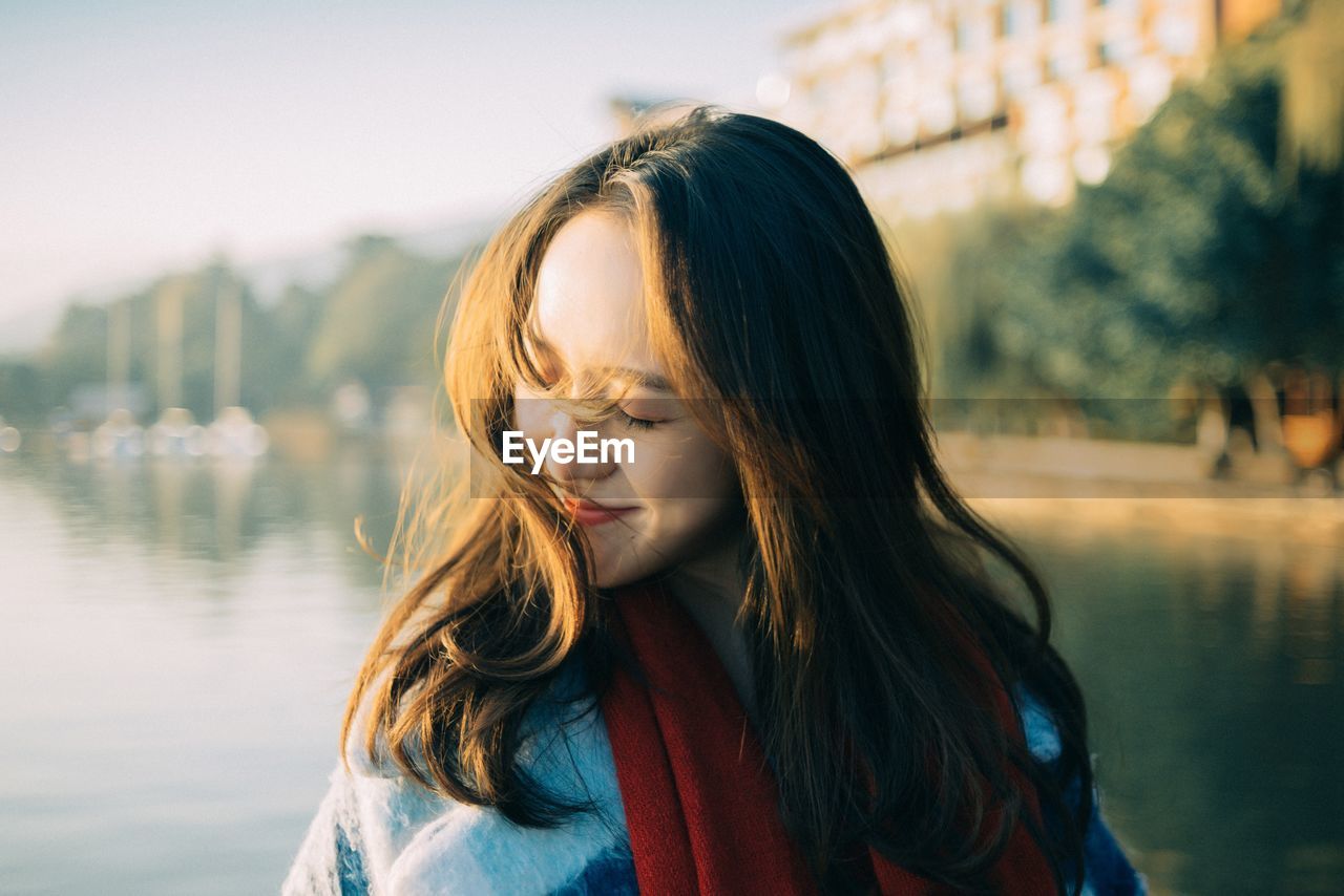 Close-up of woman smiling while standing against lake during sunset