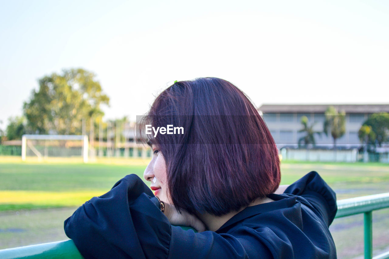 Side view of teenage girl leaning on railing against sky