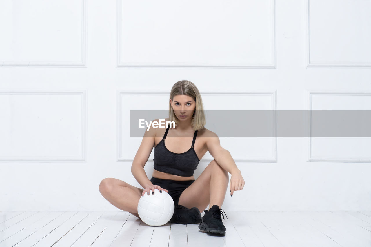 Full length portrait of woman sitting with volleyball on floor