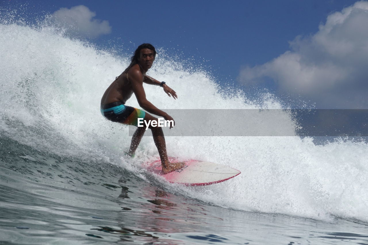 Full length of man splashing water in sea against sky