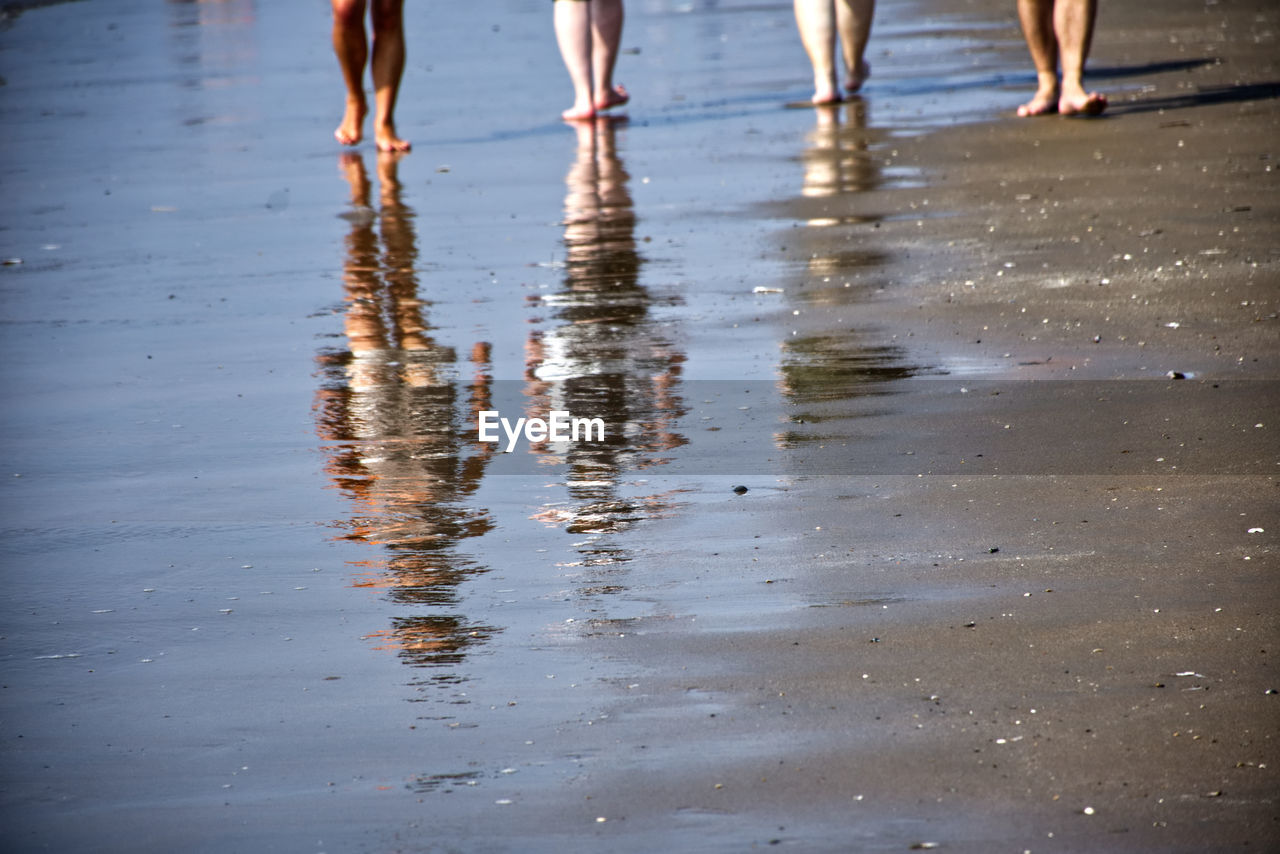 LOW SECTION OF PEOPLE WALKING ON WET SHORE