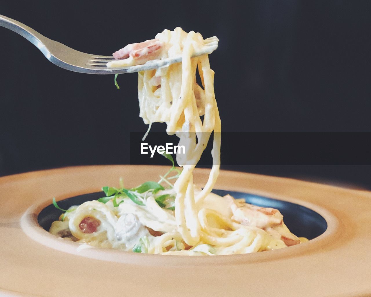 Close-up of fork with pasta in plate against black background