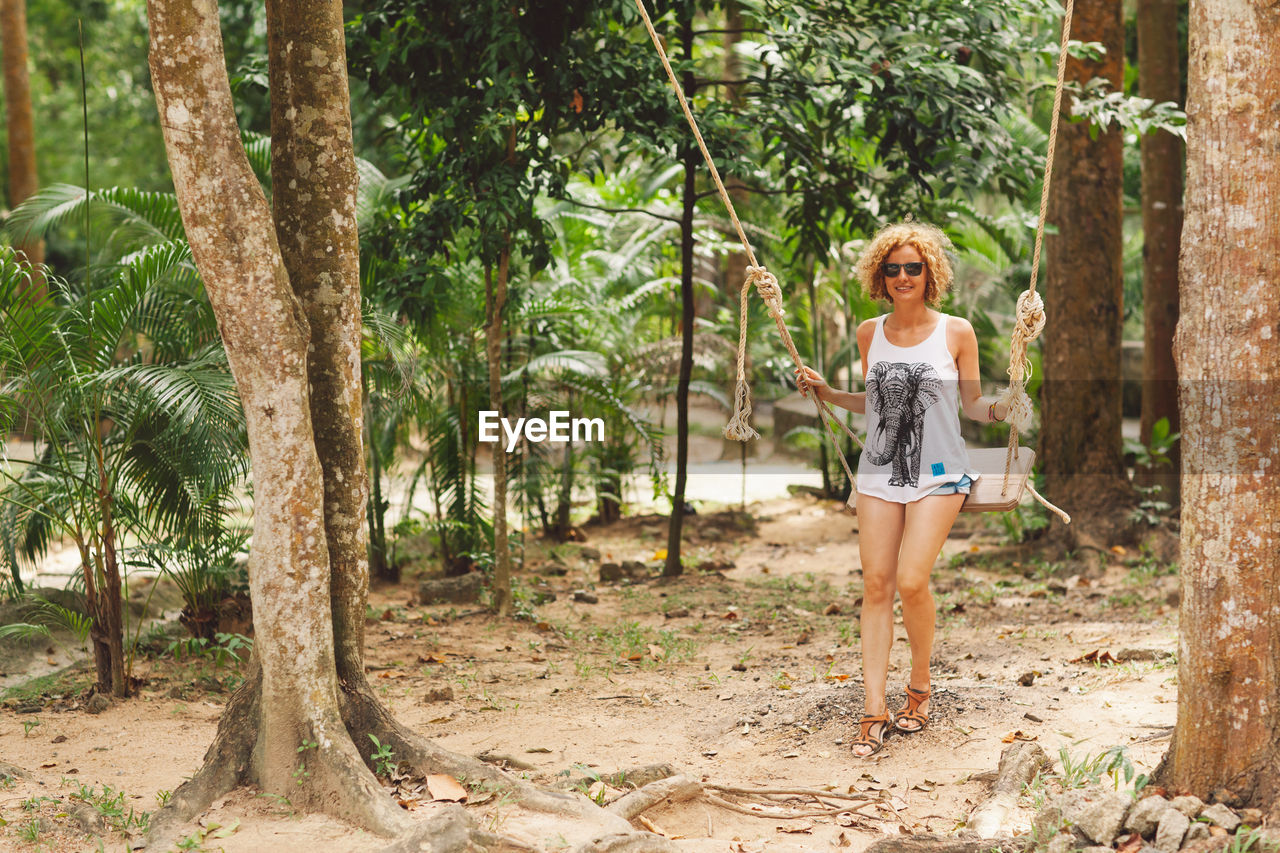 Full length portrait of smiling woman siting on swing in park