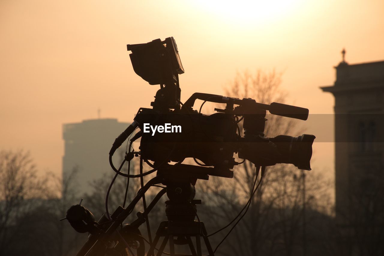 SILHOUETTE CAMERA ON FIELD AGAINST SKY AT SUNSET