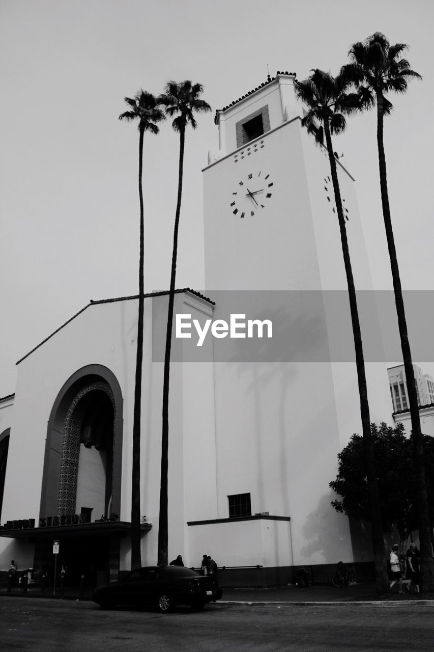 Low angle view of coconut palm trees by clock tower against clear sky