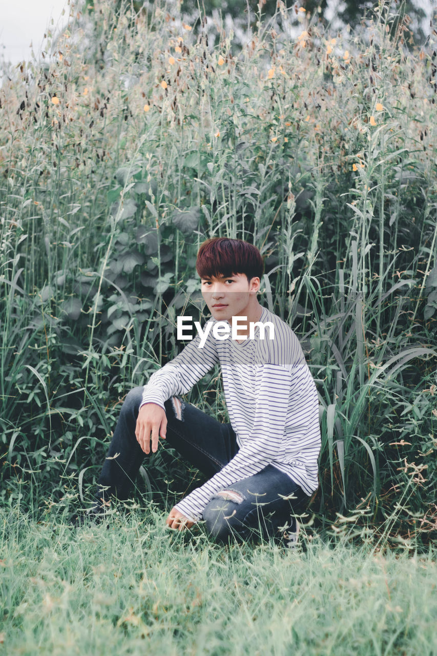 Portrait of young man kneeling against plants