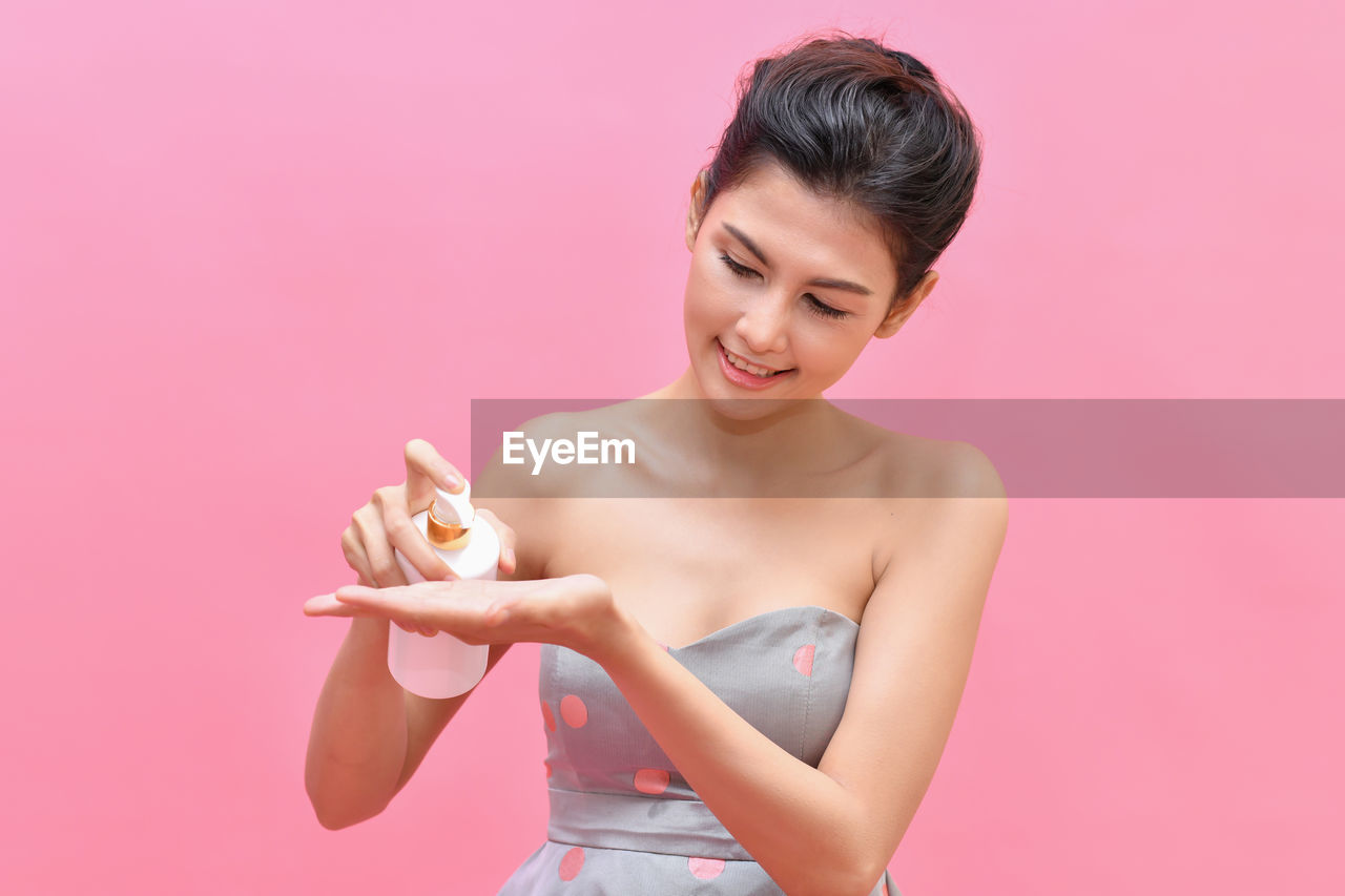 Woman pressing dispenser of cleansing foam over pink background