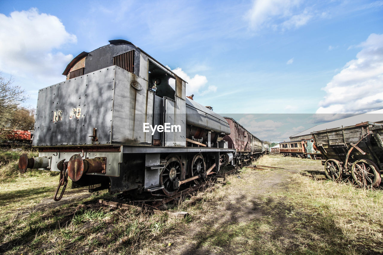 Abandoned train on field against cloudy sky