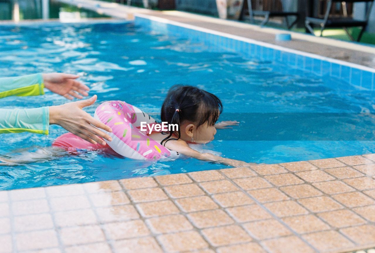Cropped hands of woman with daughter swimming in pool