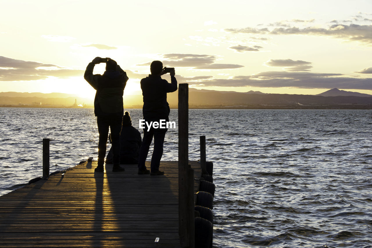 PEOPLE STANDING ON SEA SHORE AGAINST SKY