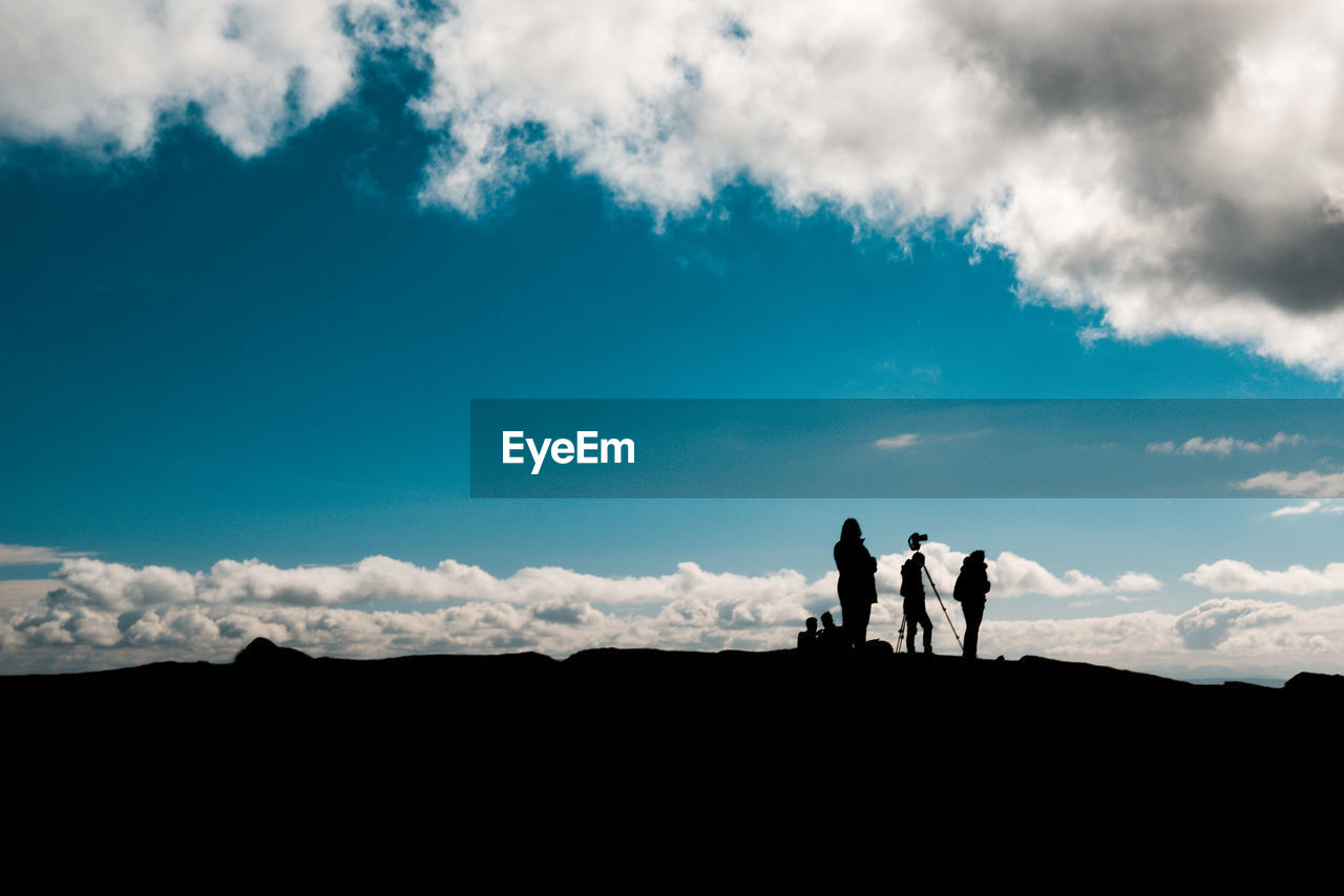 Silhouette people standing on land against cloudy sky