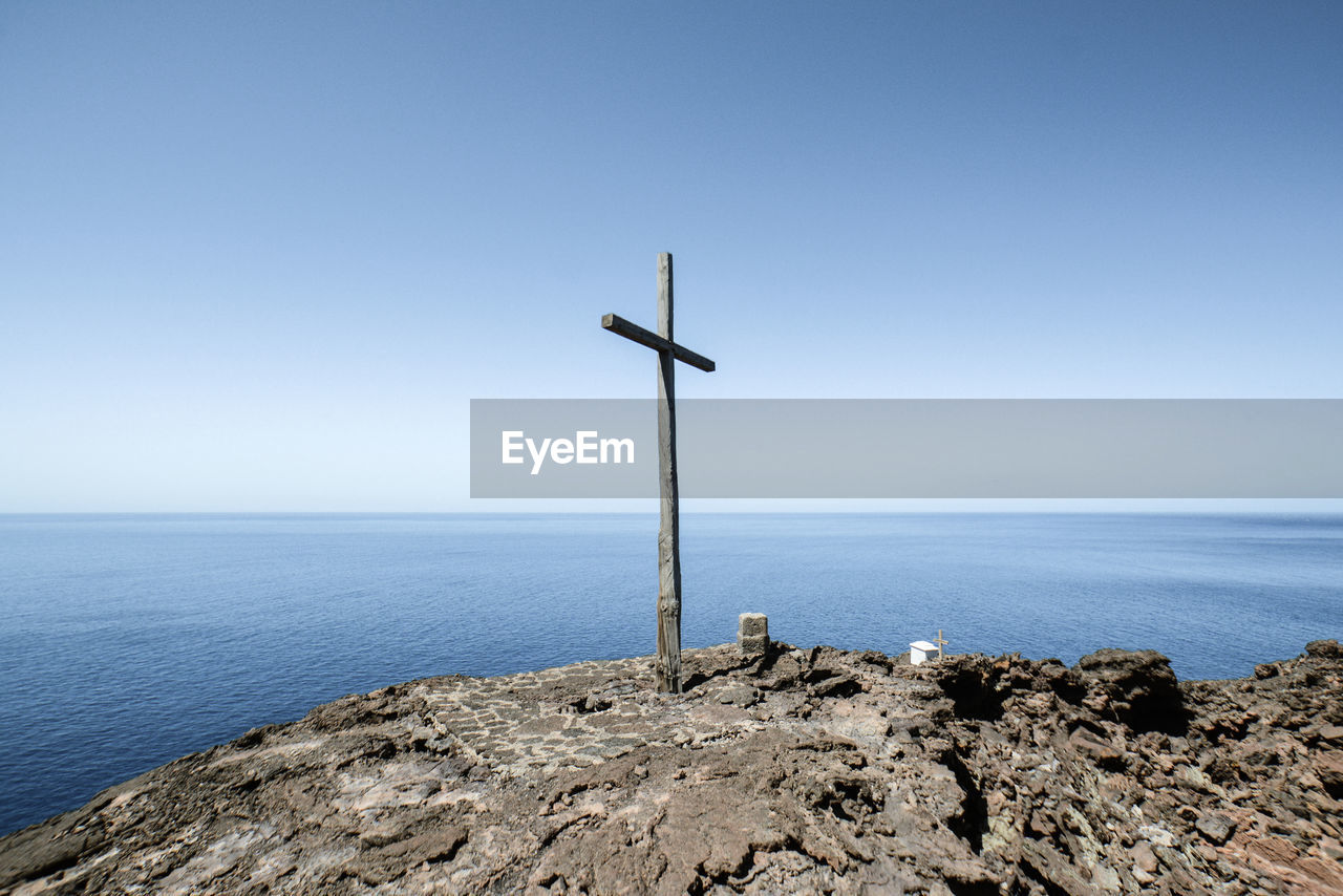 CROSS ON SHORE AGAINST CLEAR SKY