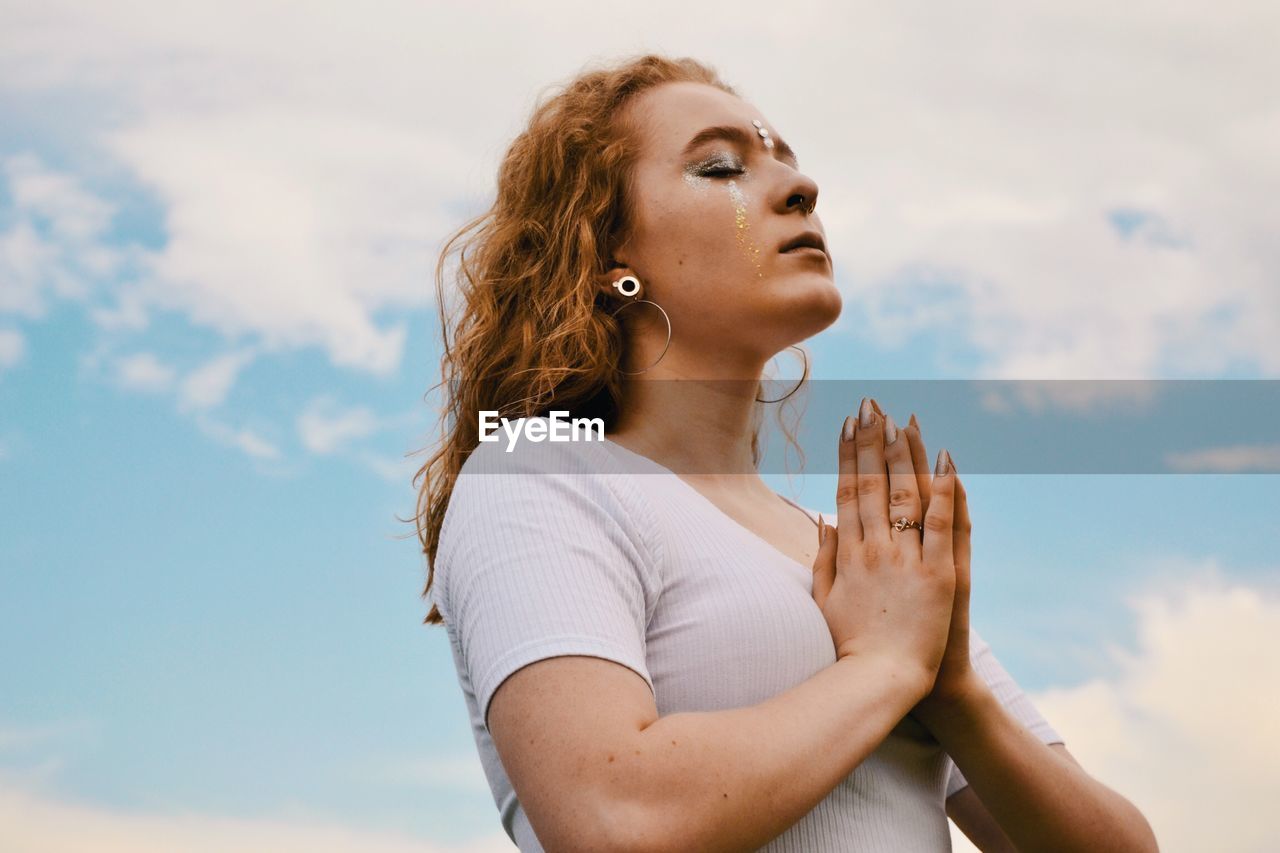 Side view of young woman meditating against sky