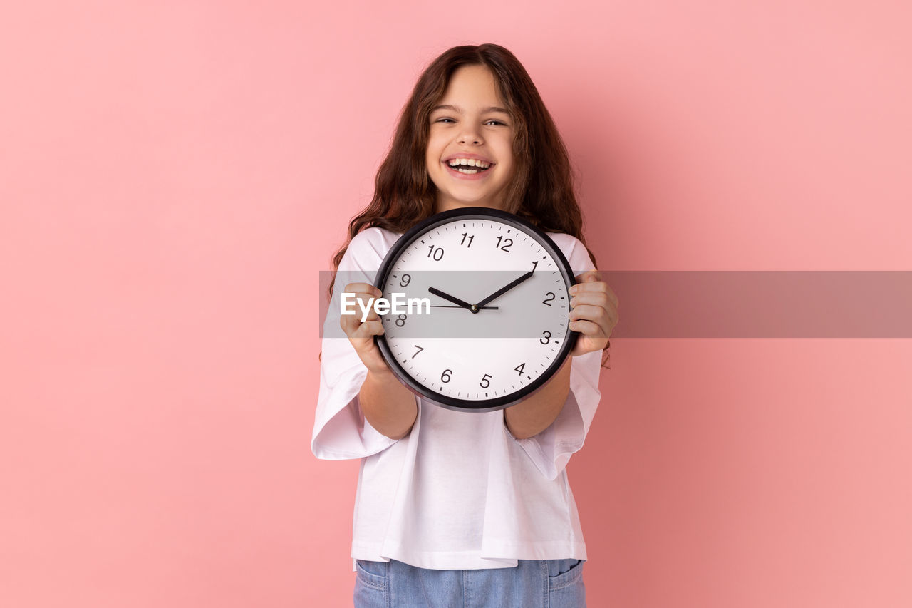 portrait of woman holding alarm clock against pink background