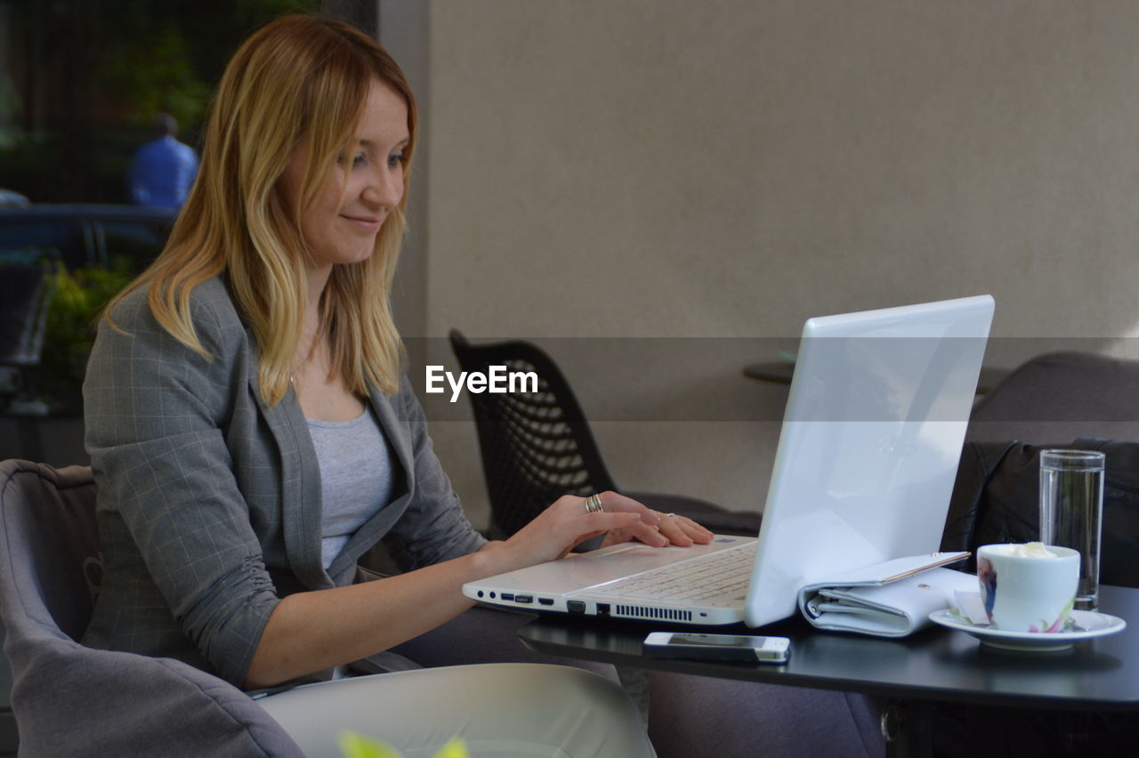 Smiling woman using laptop while sitting on chair at home