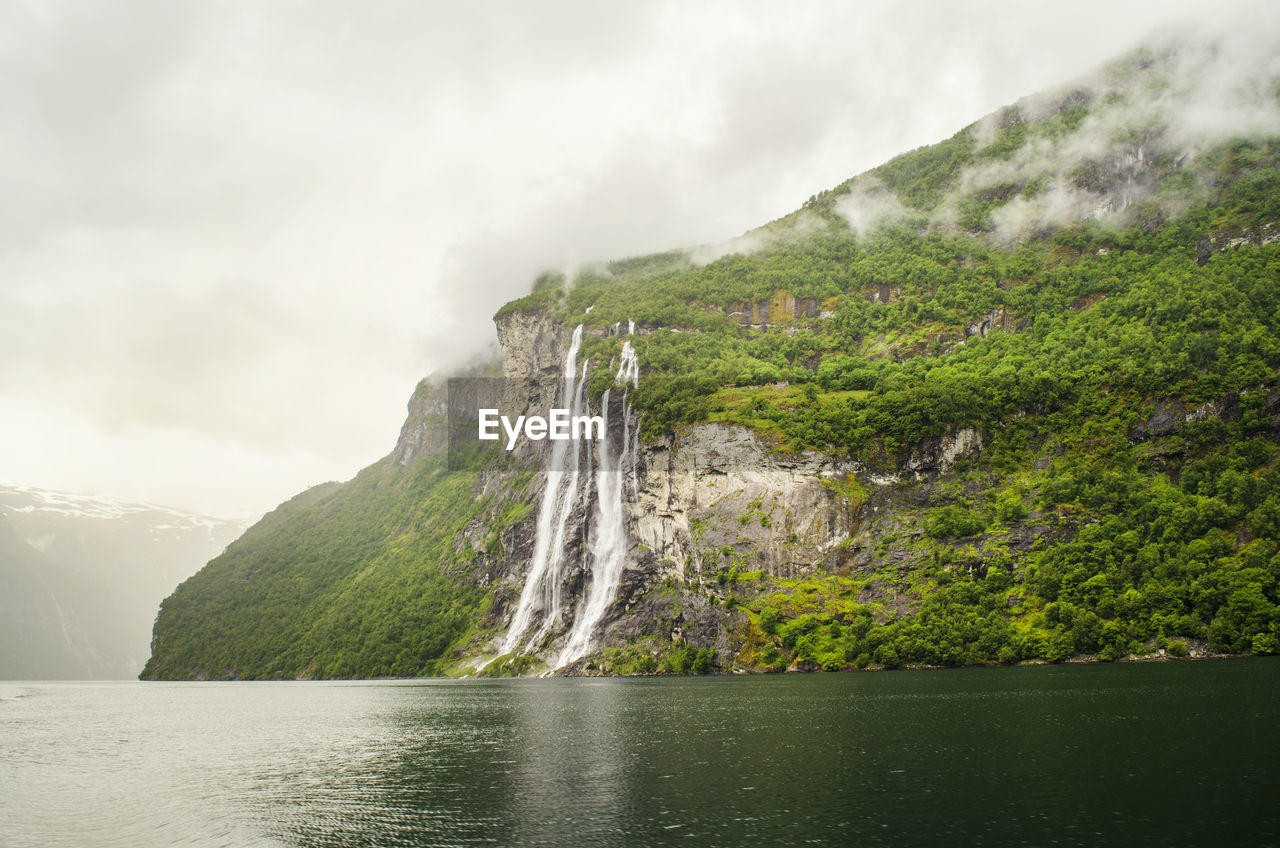 Scenic view of waterfall against mountains during foggy weather