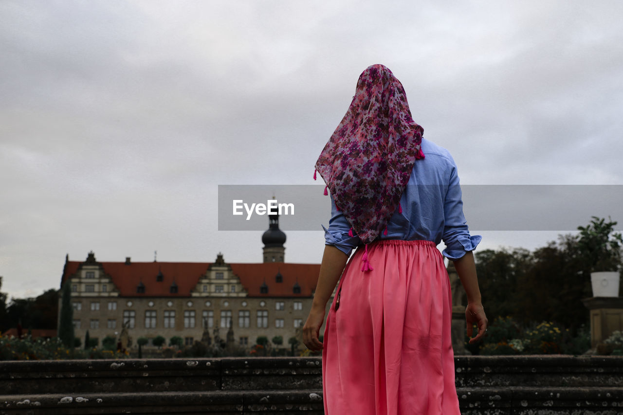 Rear view of woman standing against building and sky