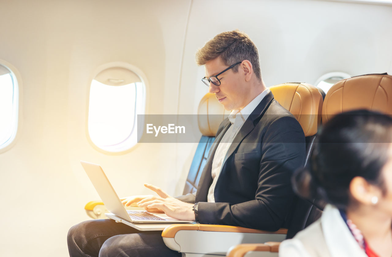 During a flight, a businessman in formal attire and glasses looks out the plane window 