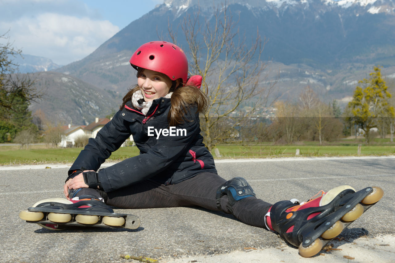 Full length portrait of teenage girl wearing inline skates sitting on road during sunny day