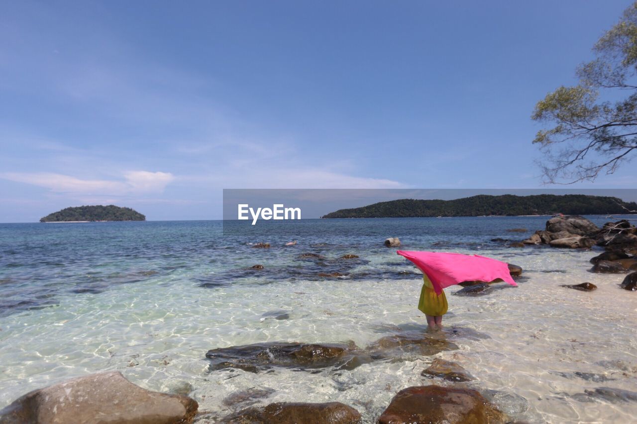 Rear view of woman holding pink sarong in sea against sky