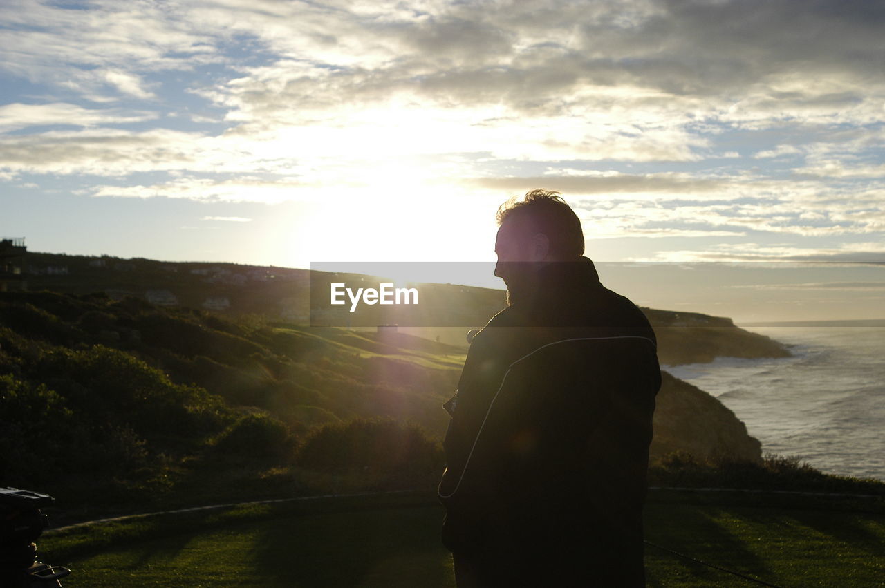 Rear view of man standing on mountain against cloudy sky during sunset