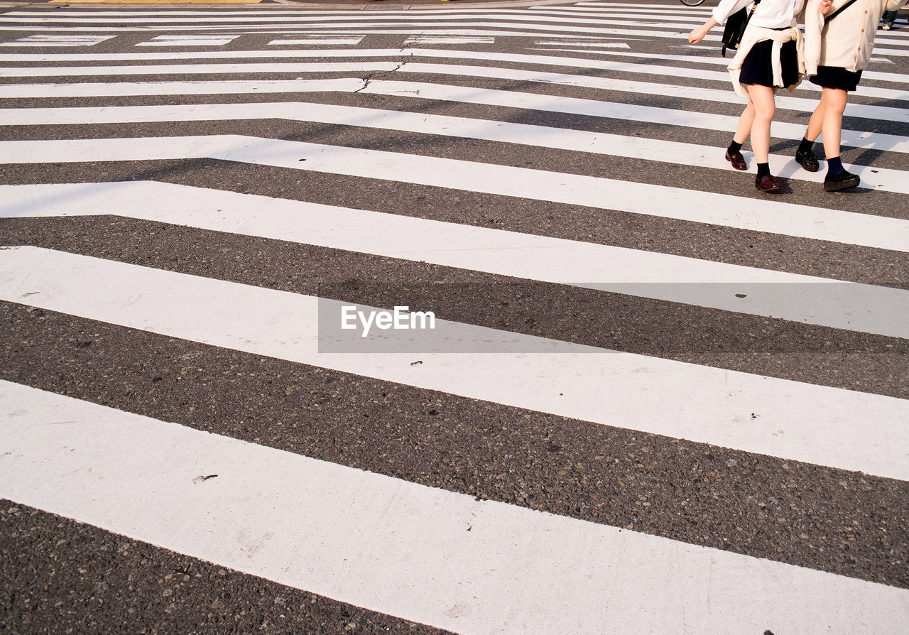 Low section of female friends crossing road in city