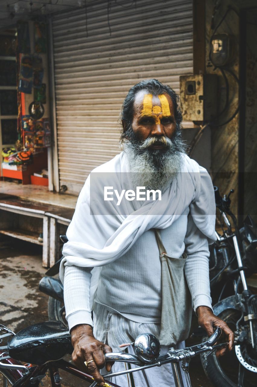 Portrait of senior man in traditional clothing with bicycle walking on street