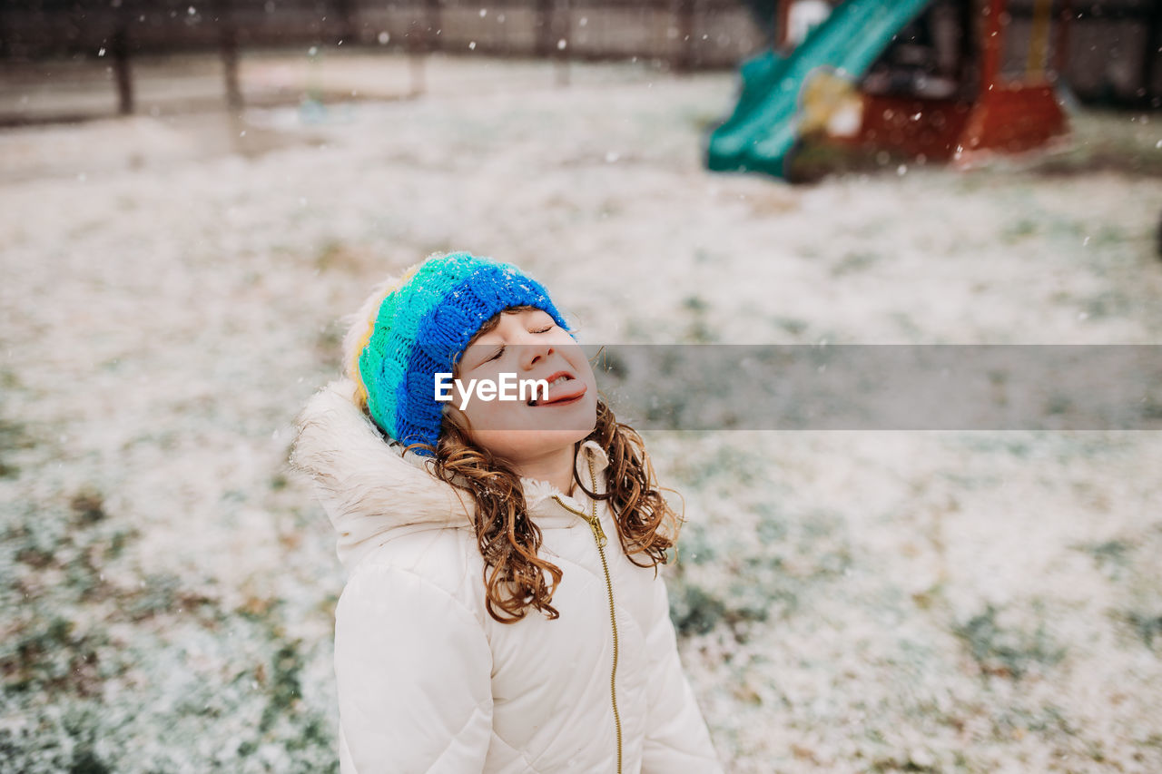Young girl standing outside catching falling snow on tongue