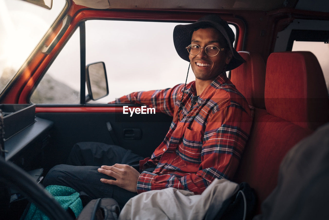 Smiling young man wearing plaid shirt while sitting in van on vacation