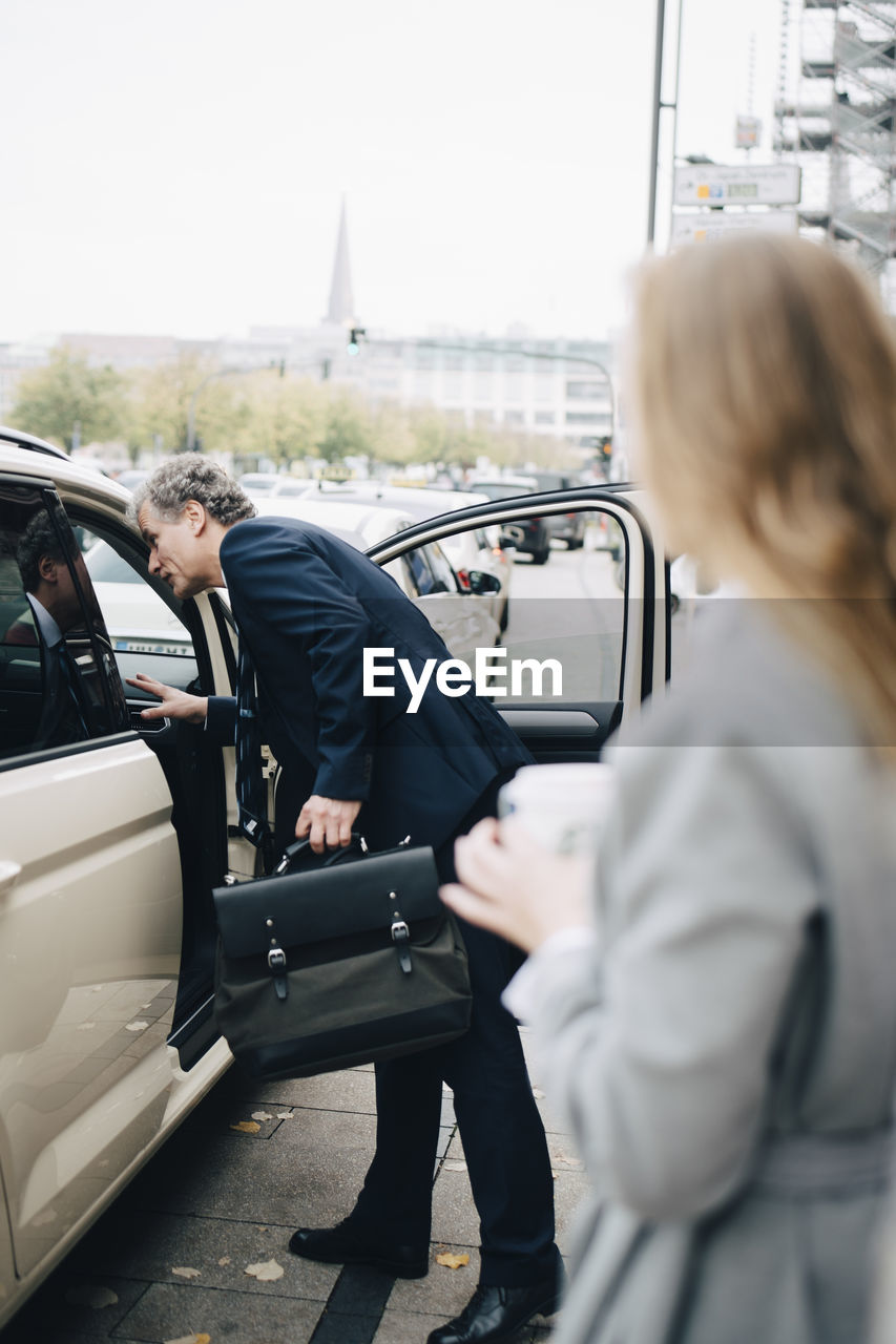 Side view of mature businessman by taxi in city