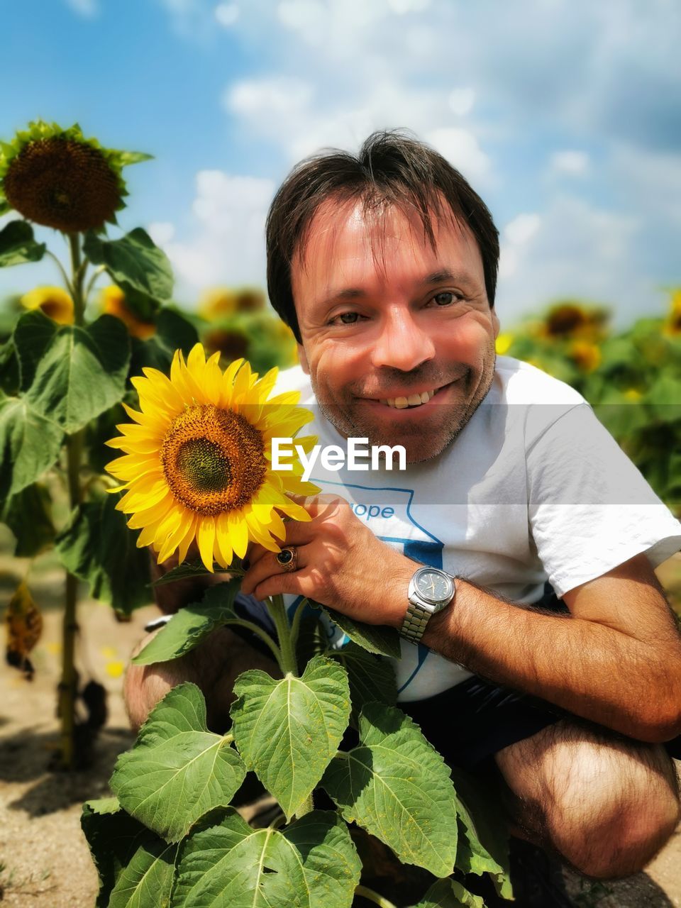 Portrait of smiling man by sunflower plants against sky