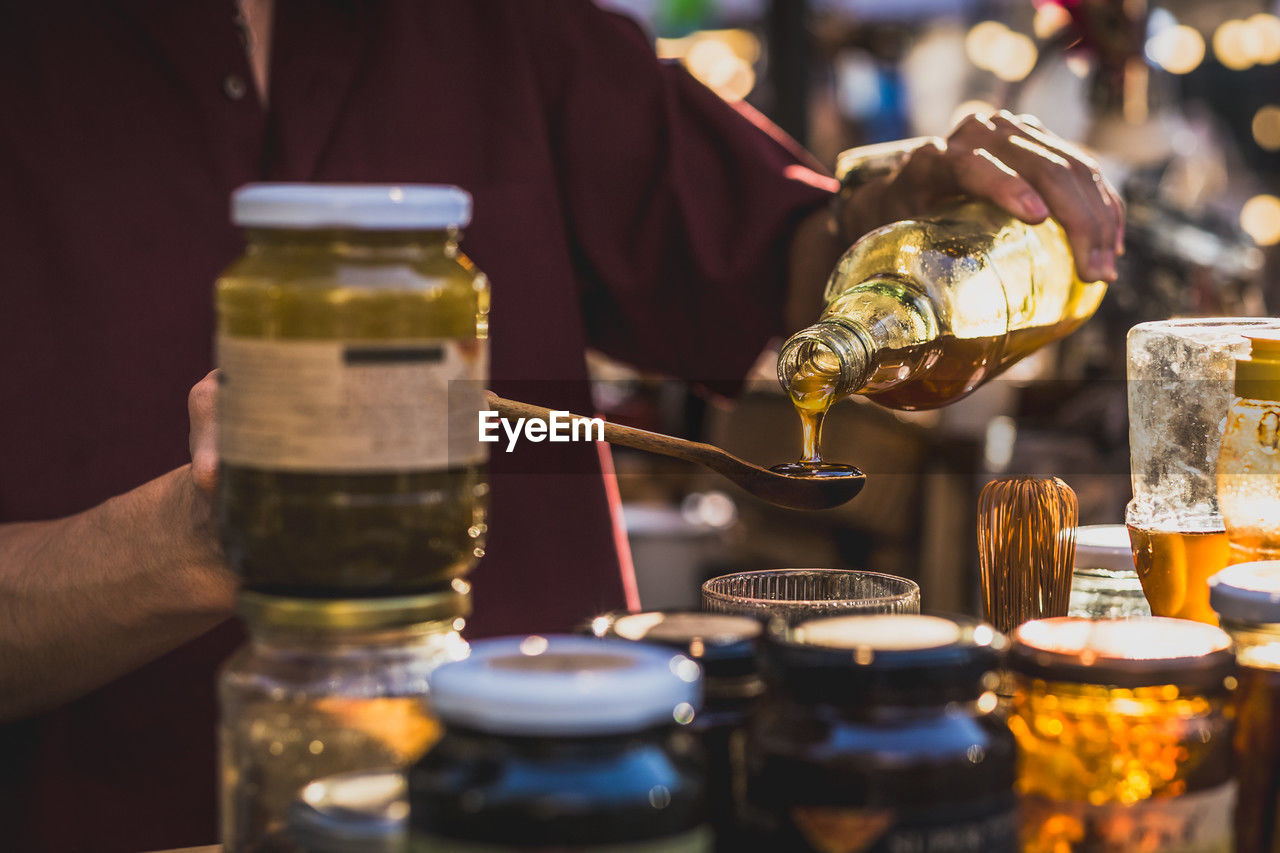 Man pouring honey from bottle into wooden spoon.