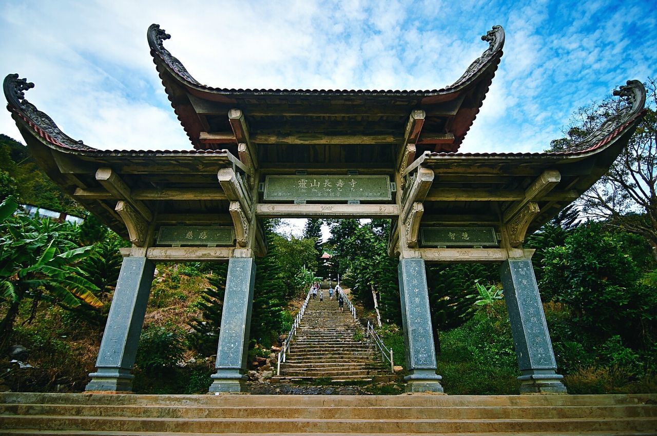 Low angle view of entrance leading towards buddha temple against cloudy sky