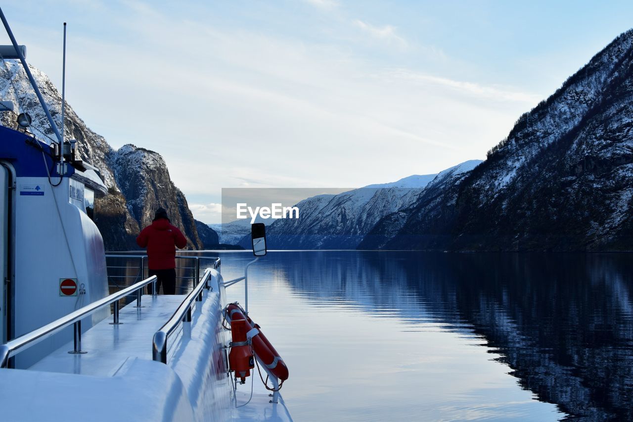 Rear view of man on yacht sailing in river amidst snowcapped mountains