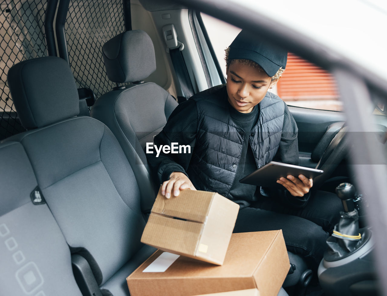 Smiling delivery person with parcel sitting in car