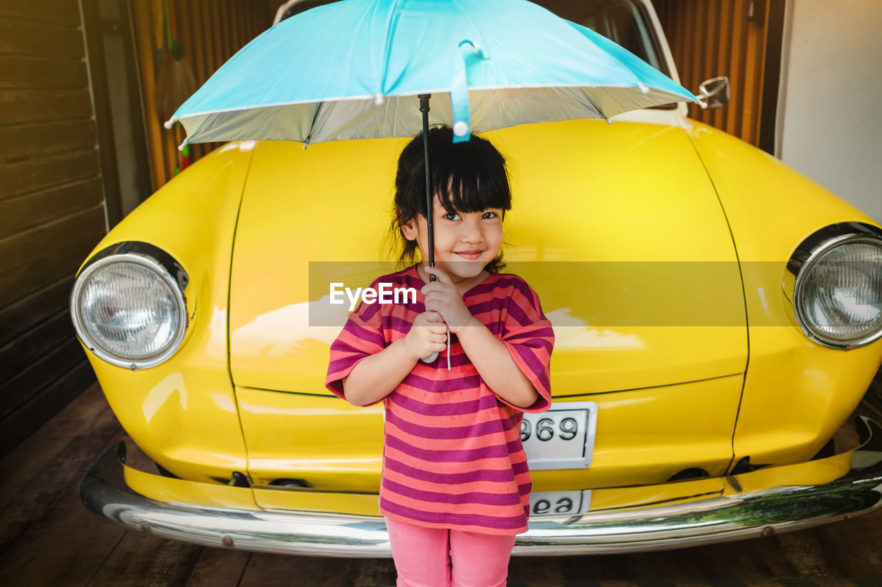 Portrait of smiling girl holding umbrella standing by vintage car