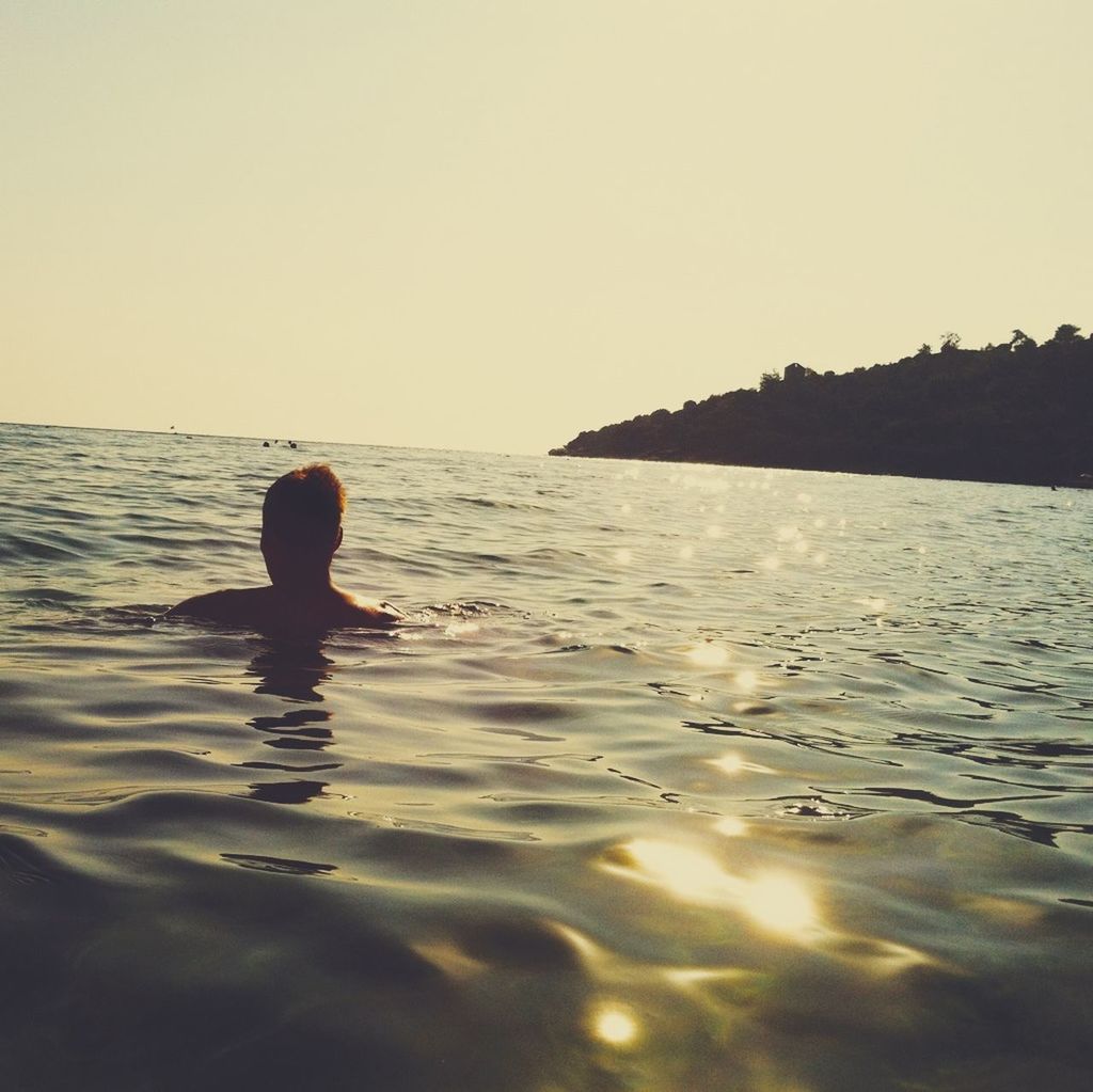 Silhouette man swimming in sea against clear sky