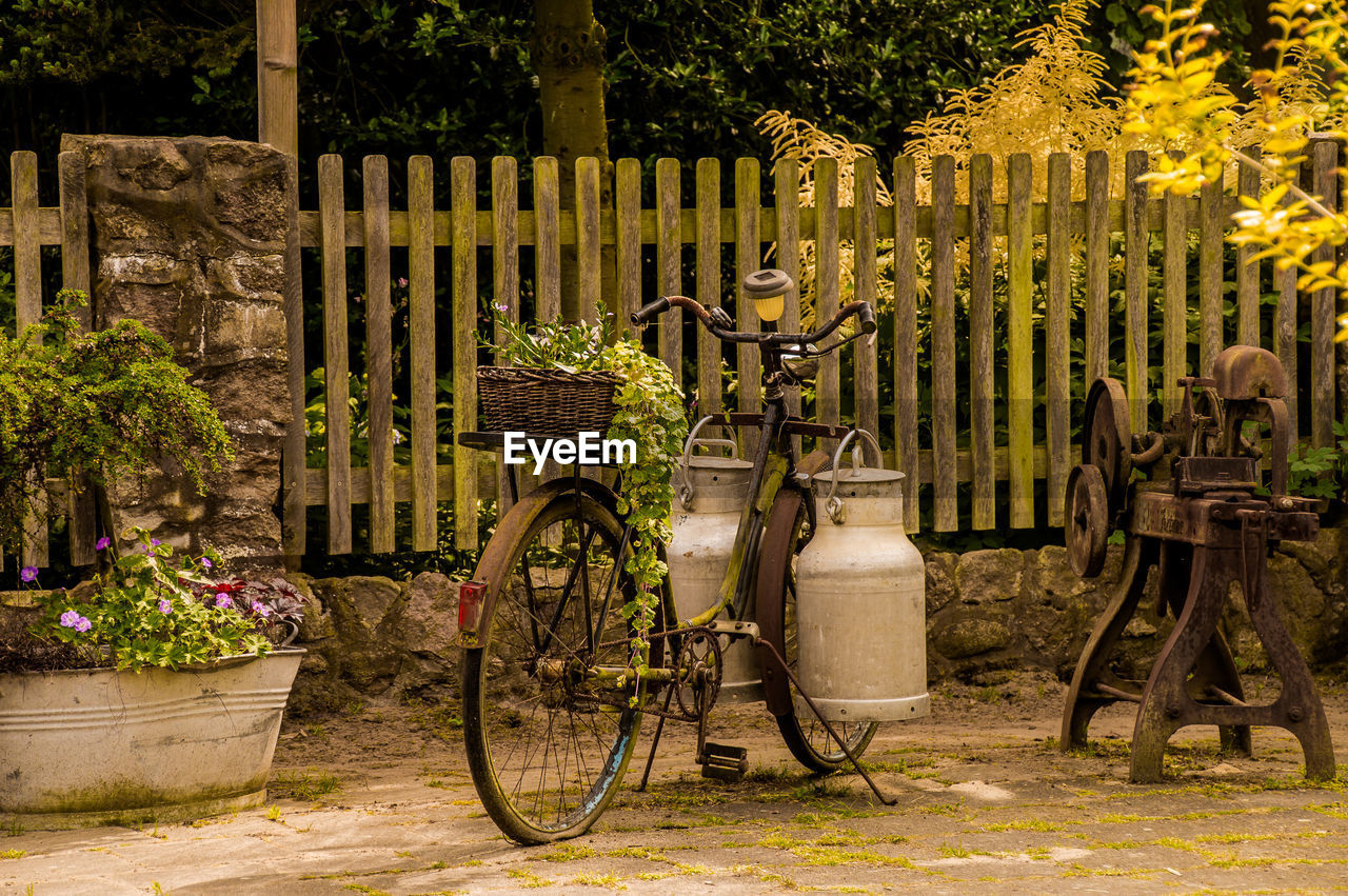 Bicycle parked on footpath by fence against trees
