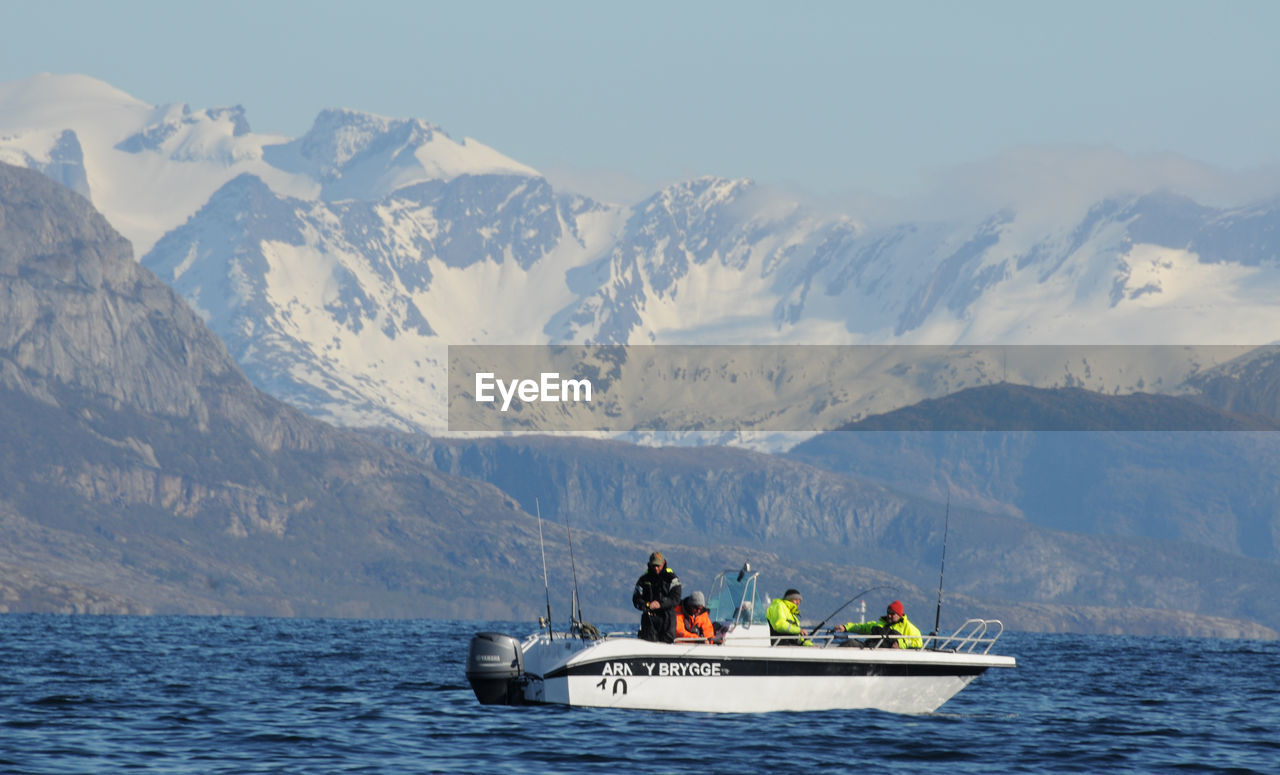 PEOPLE ON BOAT IN SEA AGAINST MOUNTAIN RANGE