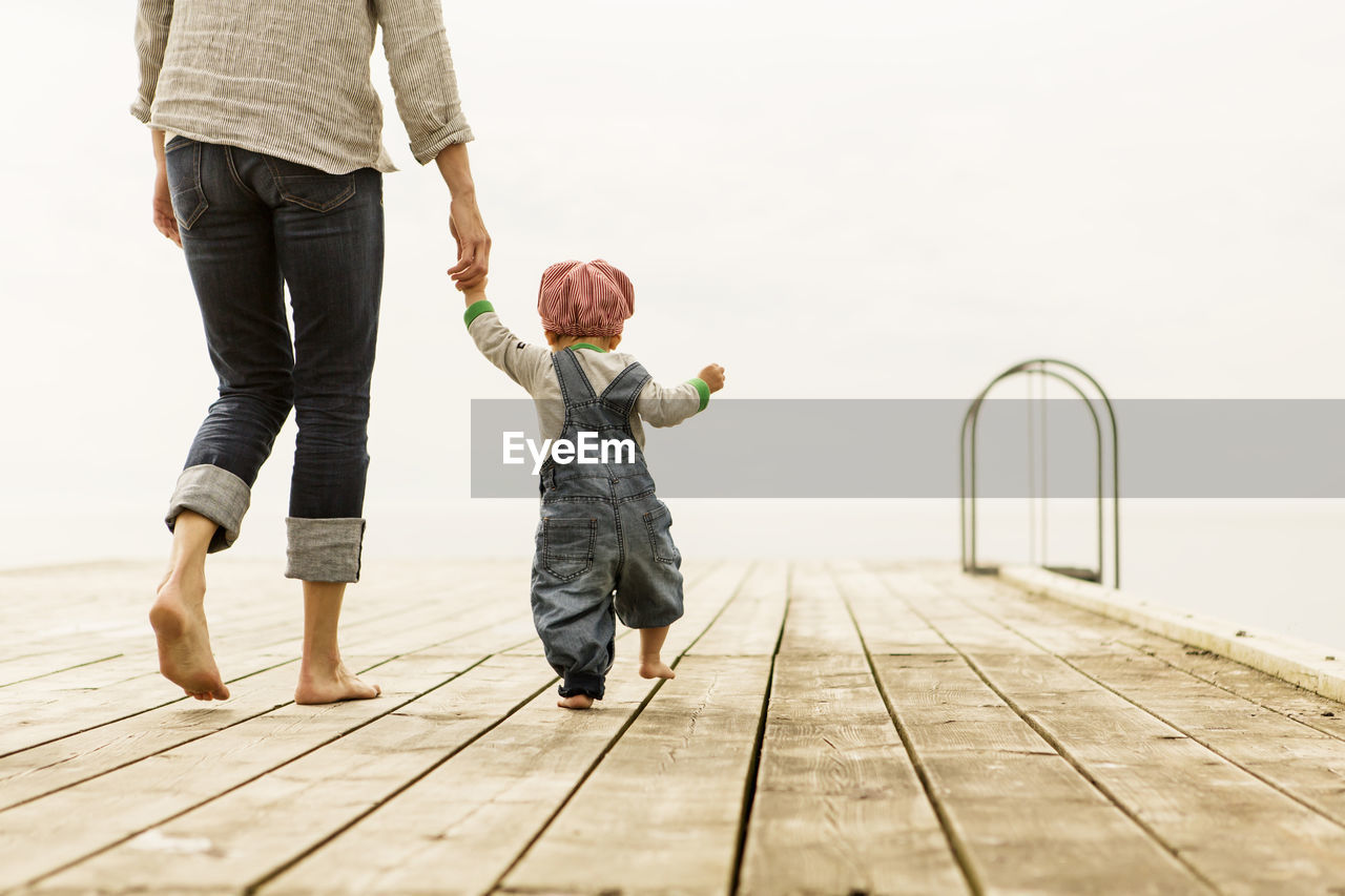 Rear view of mother walking with daughters on pier against clear sky