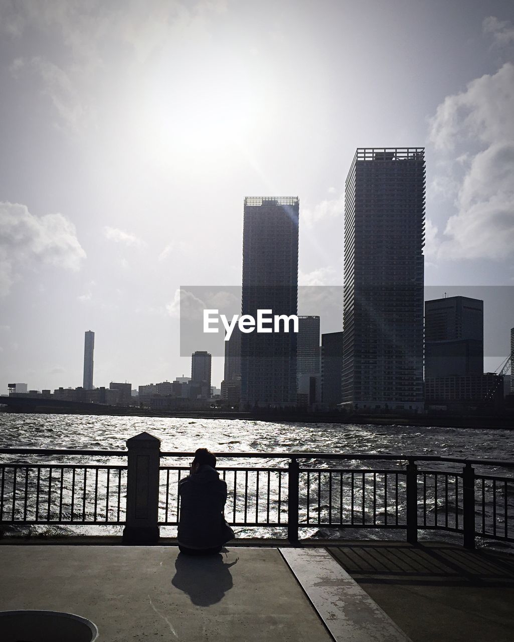Woman sitting by skyscrapers against sky