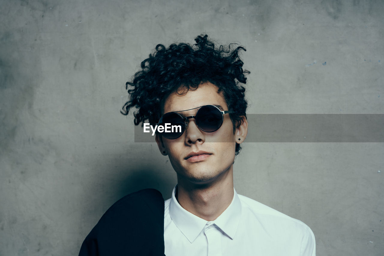 Portrait of young man wearing sunglasses standing against wall