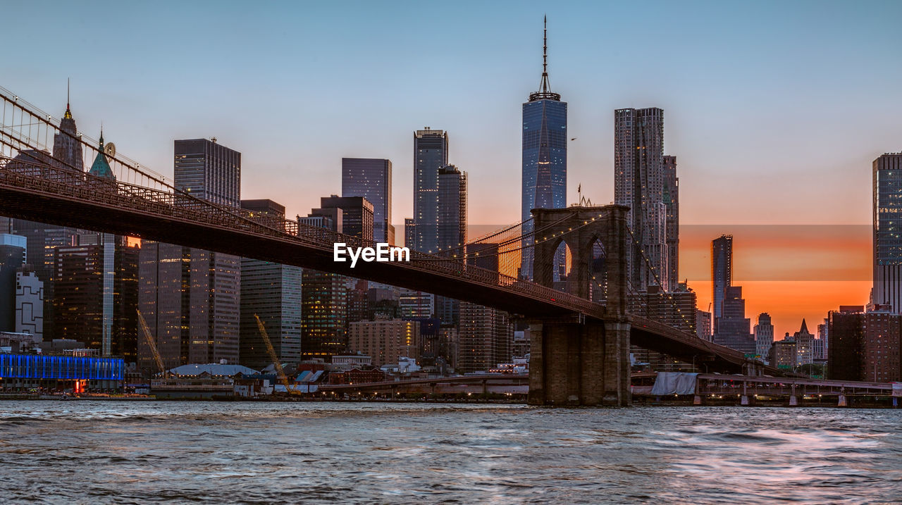 Bridge over river by buildings against sky in city