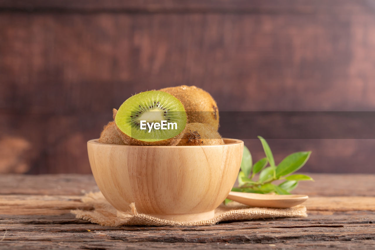 A half of kiwi in a wood bowl on the table. spoon on the brown sack