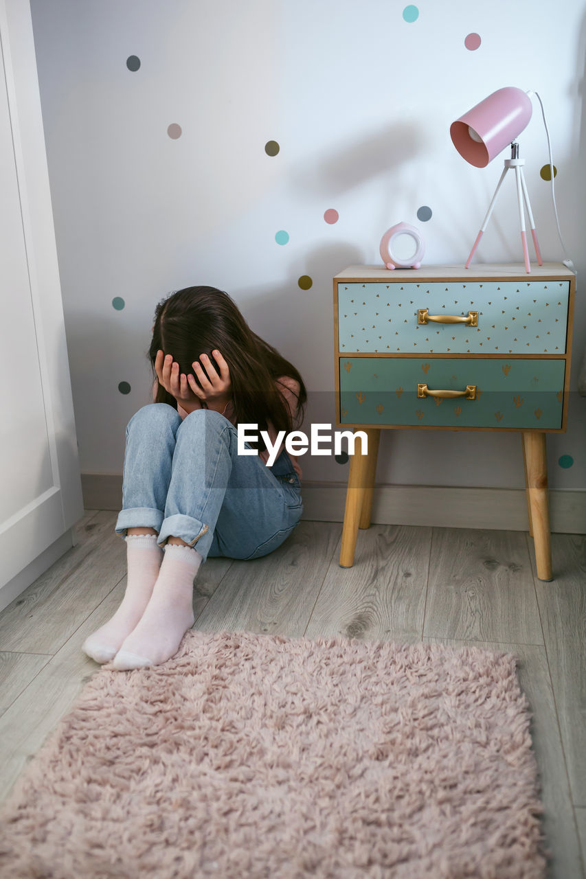 Unrecognizable little girl covering her face with hands sitting on the floor