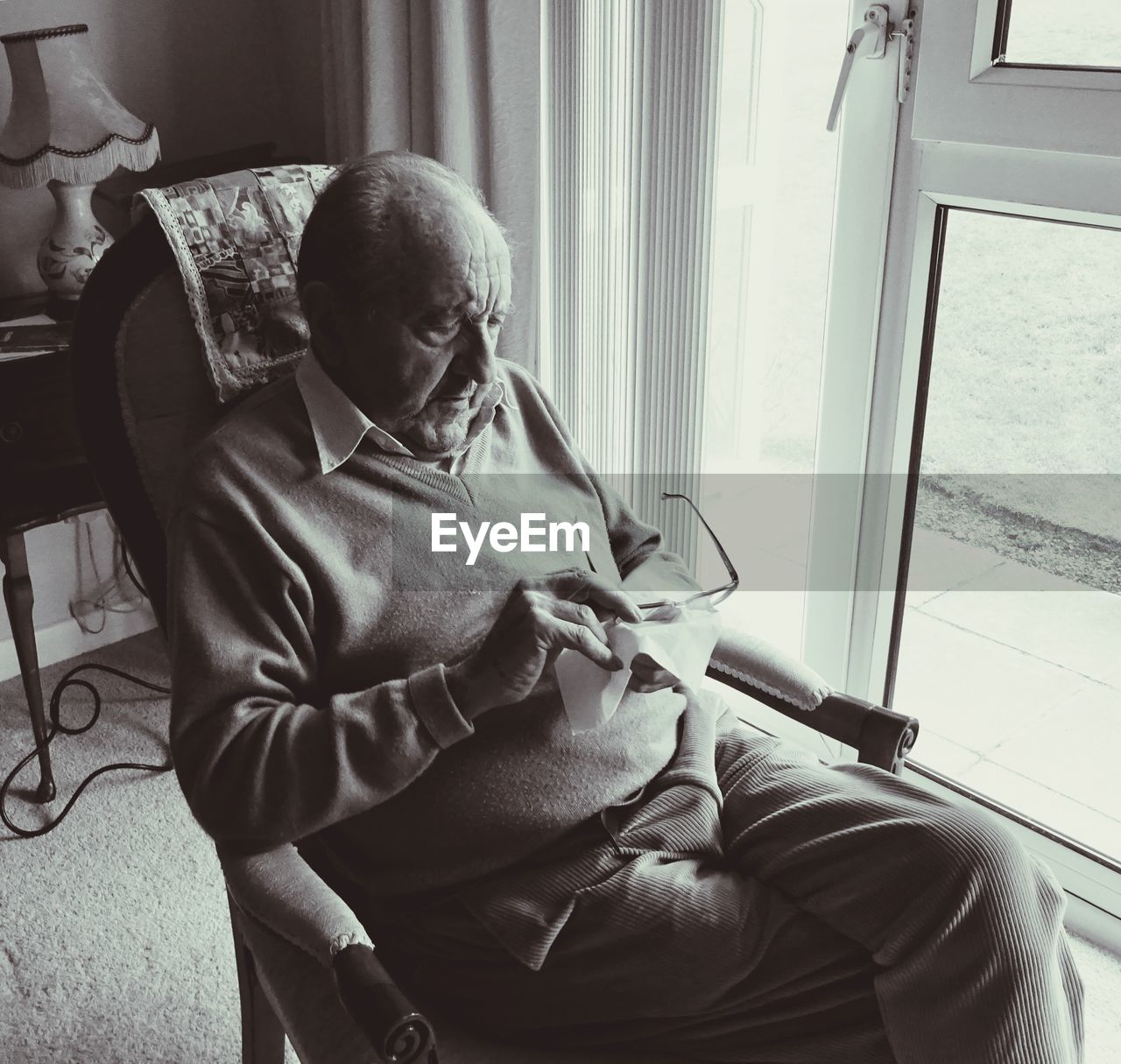 High angle view of senior man cleaning eyeglasses while sitting on armchair