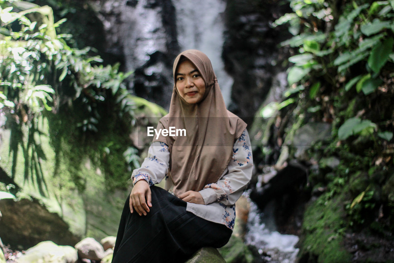 Portrait of young woman sitting on rock in forest