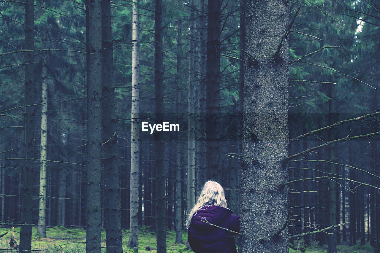 Woman standing by tree trunk in forest